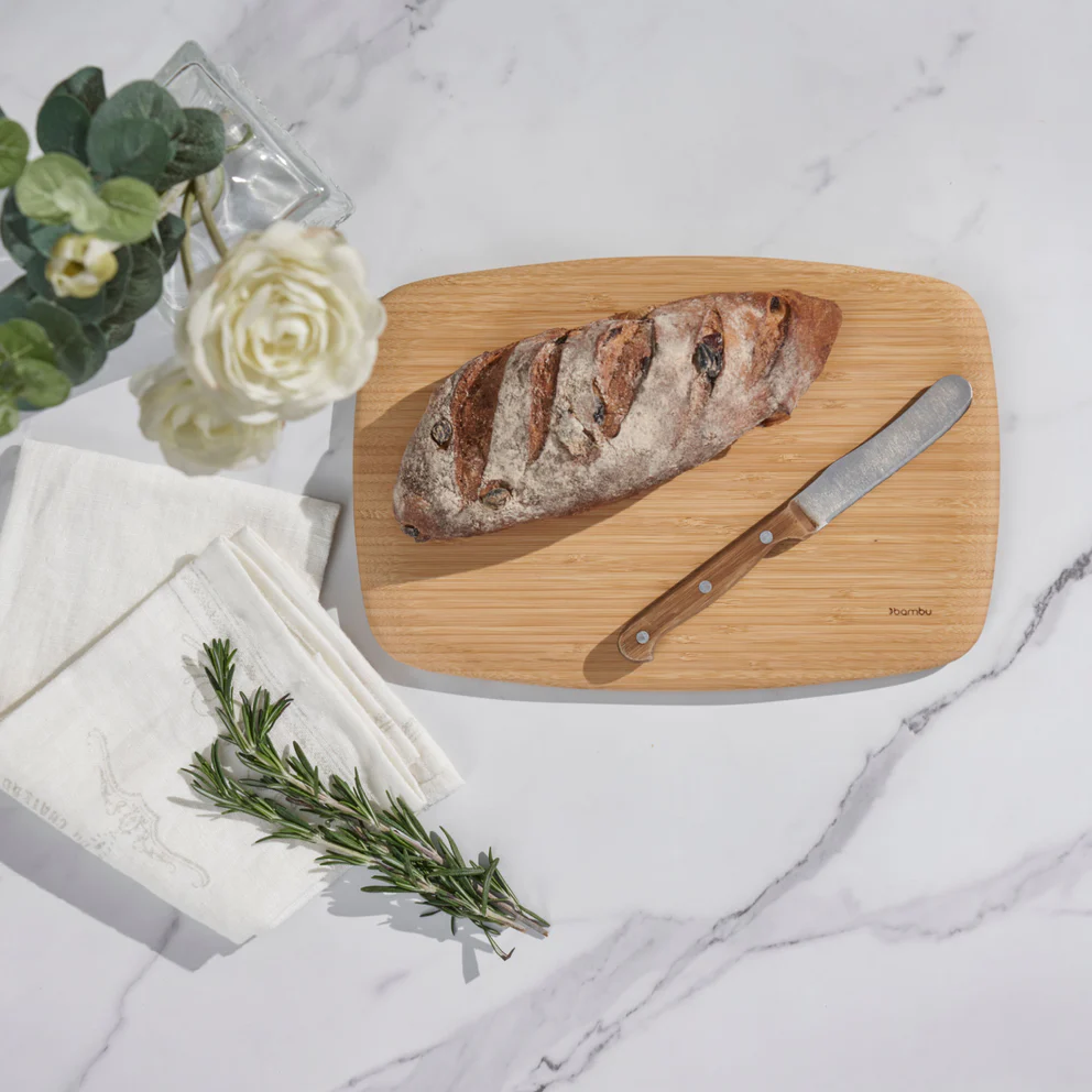 a bamboo cutting board with a loaf of bread, a non toxic kitchen utensil